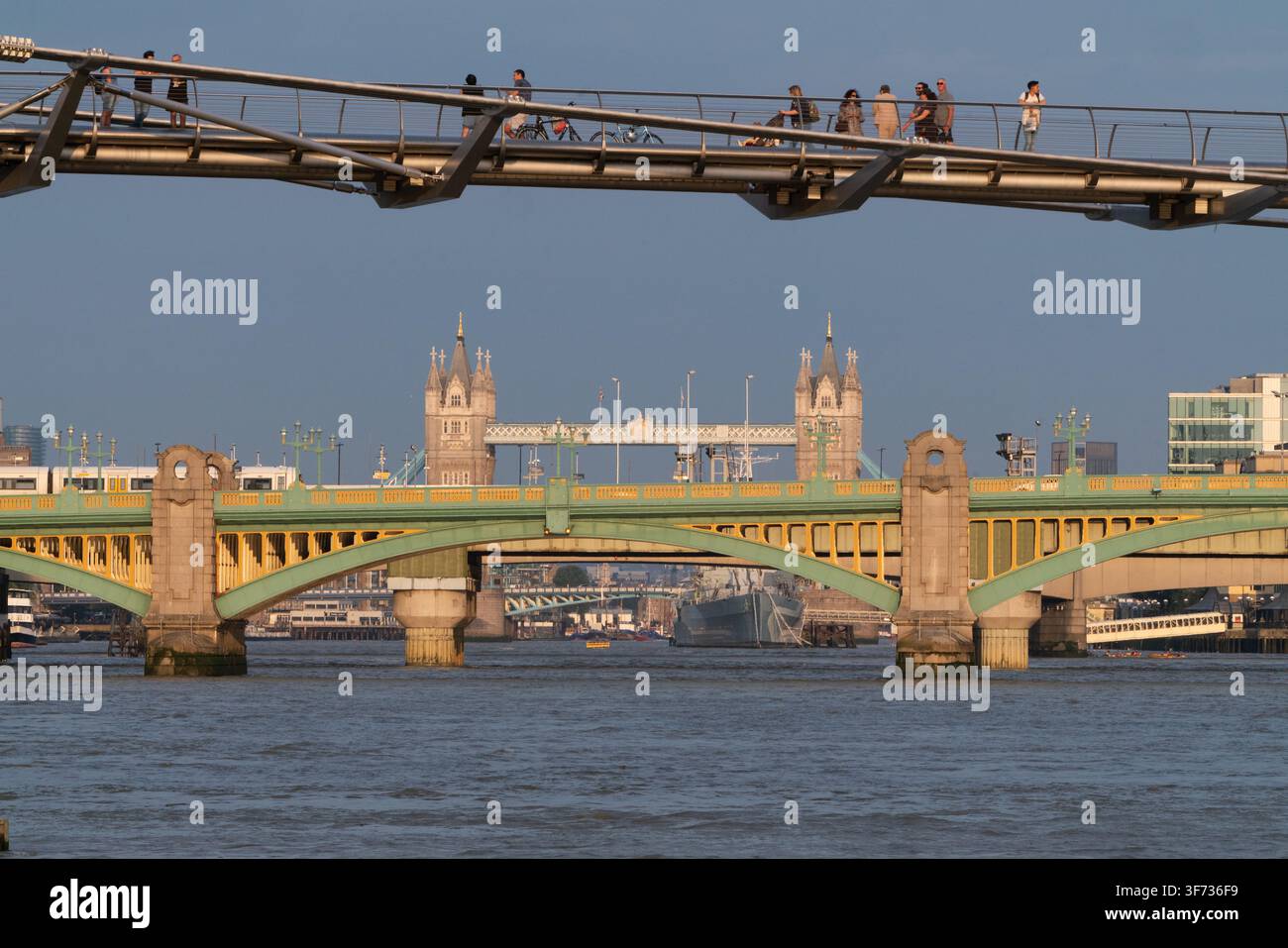 Menschen überqueren die Millennium Bridge bei Sonnenaufgang in Southwark, mit Blick auf die Southwark Bridge und die Tower Bridge an der Themse. Stockfoto
