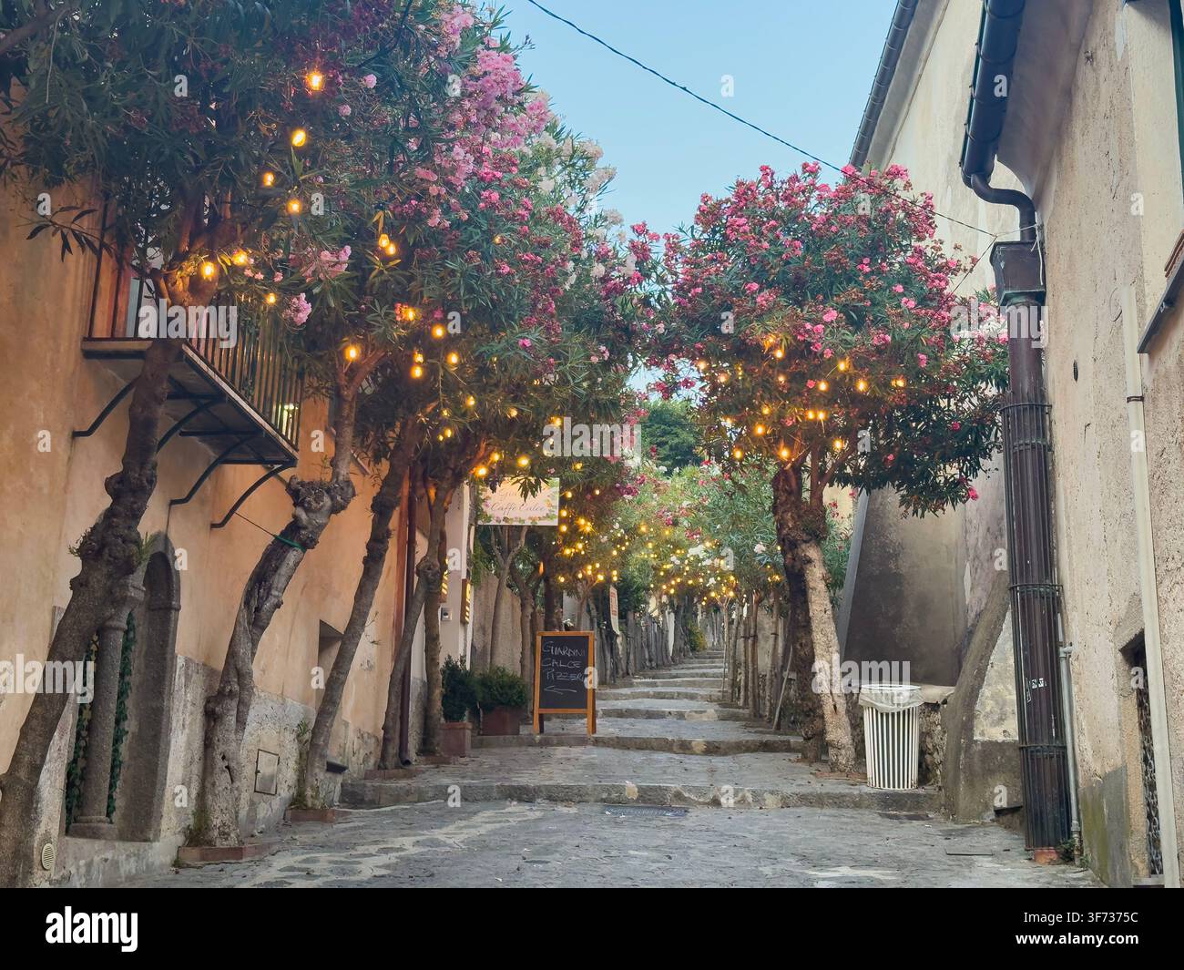 Blühende Oleanderbäume und glühende Lichter säumen eine malerische steinerne Treppe durch die historische Hügelstadt Ravello an der Amalfiküste in Italien. - Smartphone-aufgenommenes Stockfoto