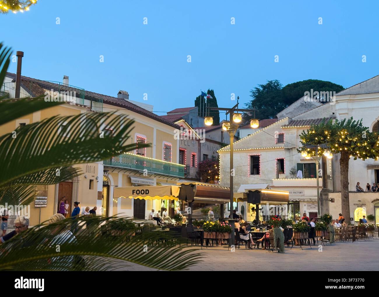 Piazza Duomo von Ravello mit Restaurants und historischen Gebäuden, die bei Abenddämmerung an einem Sommerabend beleuchtet sind, Amalfiküste, Kampanien, Italien. - Smartphone-aufgenommenes Stockfoto