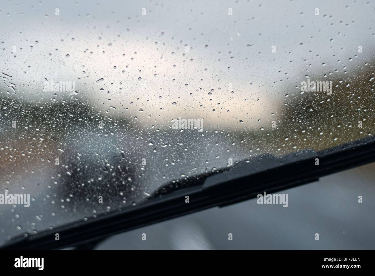 Nahaufnahme eines Wassertropfens auf der Windschutzscheibe mit schwarzer Wischerlippe unten an einem bewölkten Tag Stockfoto