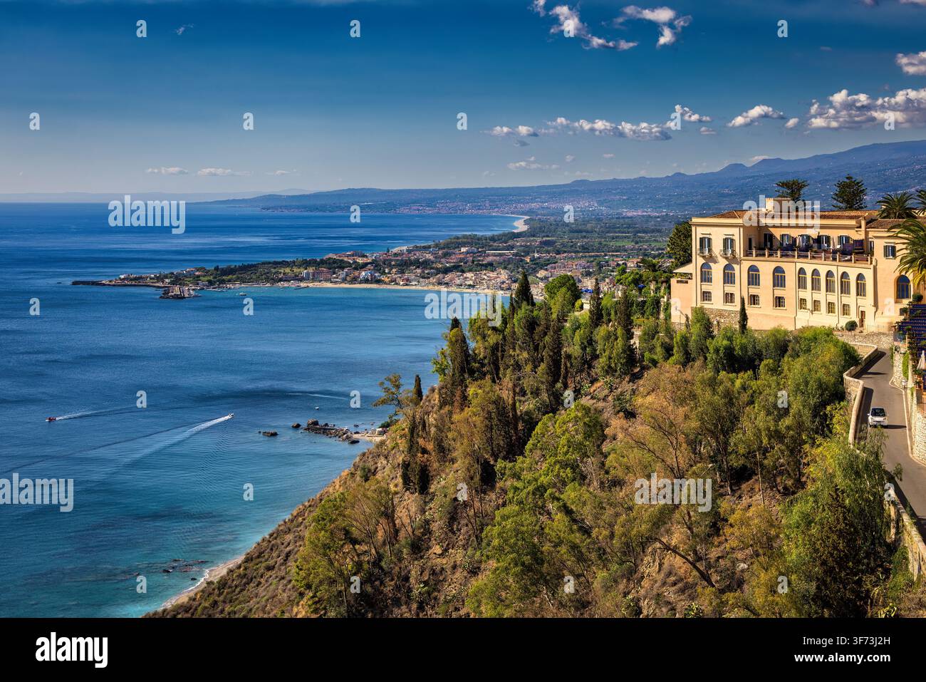 Erhöhte Ansicht von Taormina entlang der ionischen Küste Siziliens, mit Giardini Naxos in der Ferne neben dem blauen Mittelmeer sichtbar. Stockfoto
