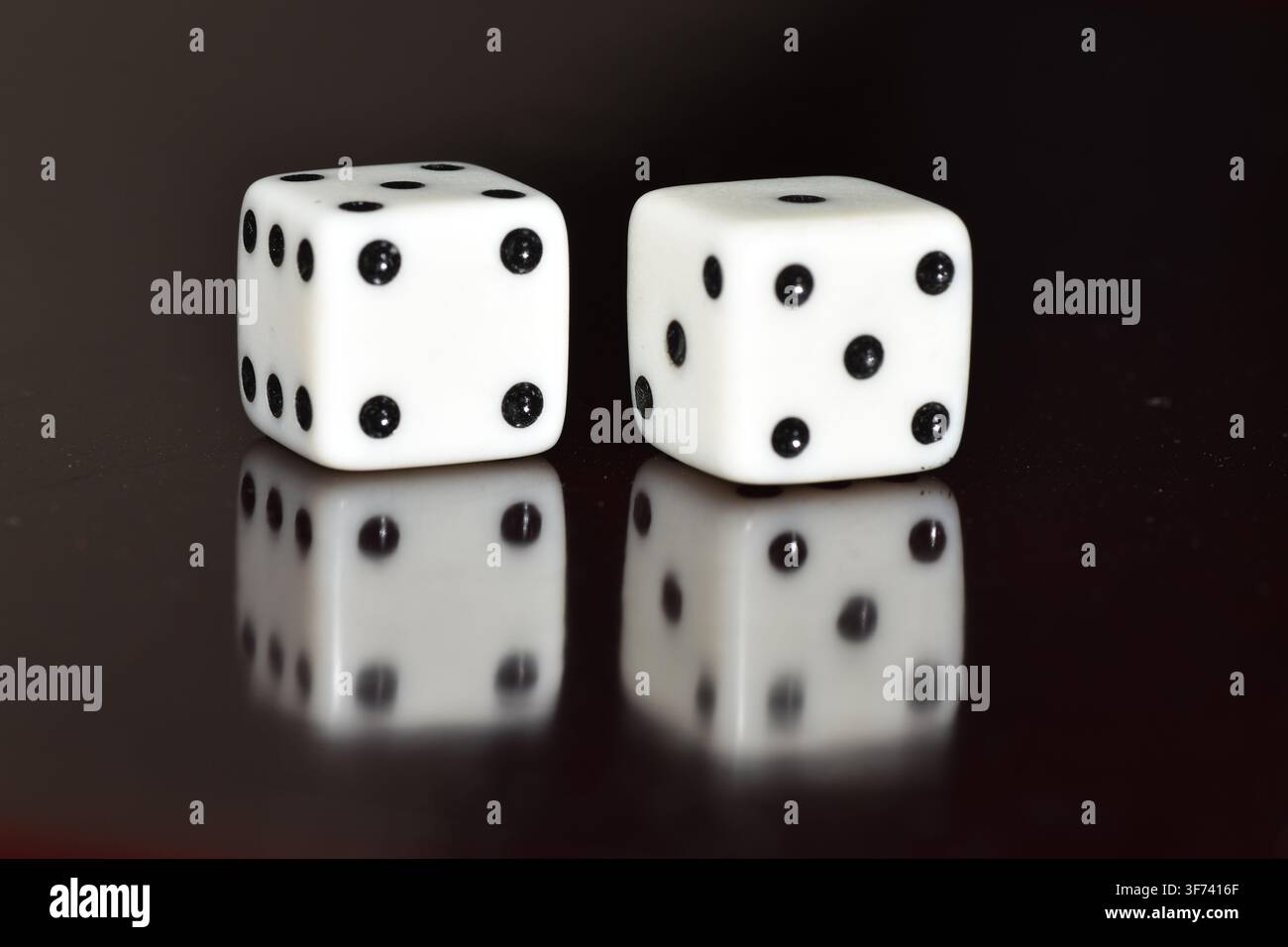 Ein Paar weißer, sechsseitiger Würfel, die auf einer glänzenden schwarzen Oberfläche mit einem klaren Spiegelbild ruhen, mit einer Gesamtzahl von sieben-4 links und 5 rechts. Stockfoto