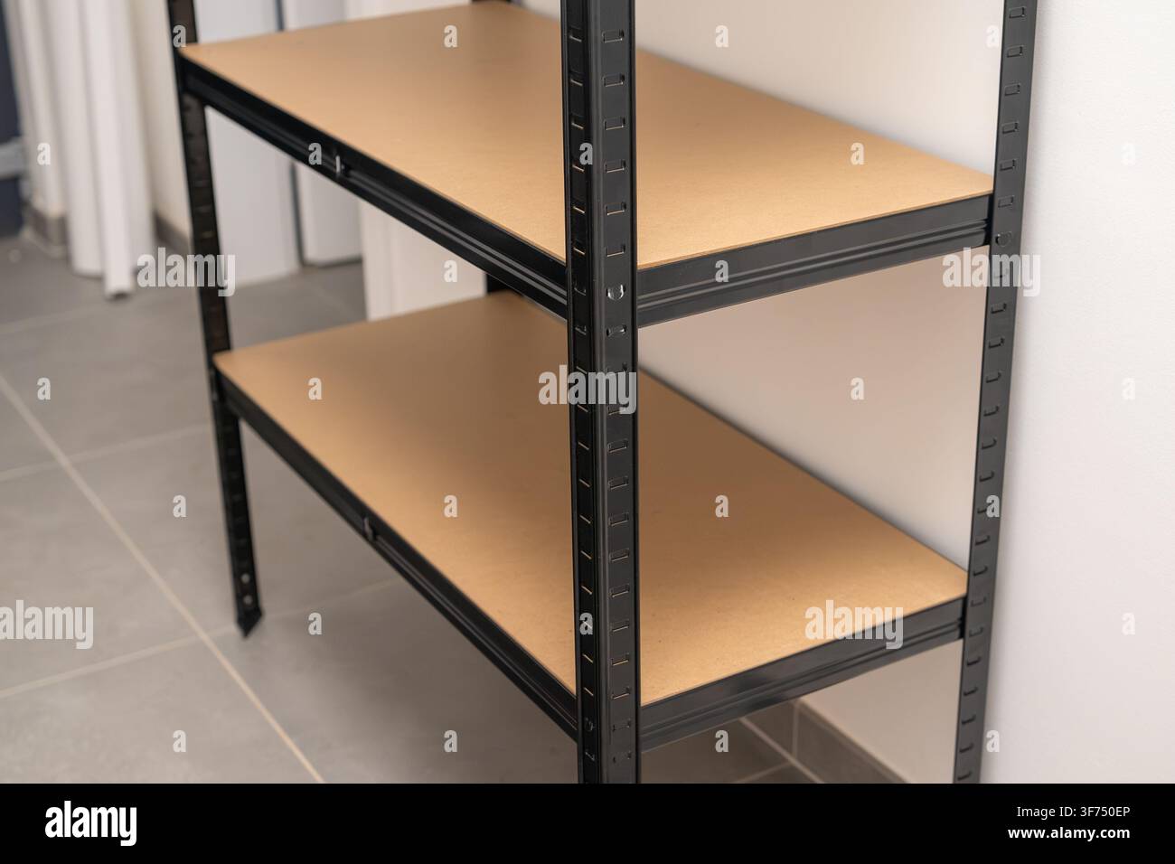 Schwerlast-Industrieregalkonstruktion mit schwarzem Metallrahmen und stabilen Holzregalen. Die Einheit ist in einer minimalistischen Lagerumgebung positioniert, mit einem sauberen Fliesenboden und neutralen Wandfarben. Stockfoto