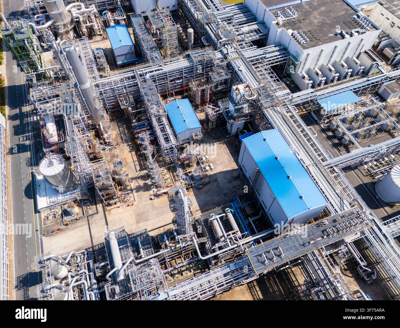 Vertikale Luftaufnahme eines großen petrochemischen Industriekomplexes mit blau bedachten Gebäuden, dichten Rohrnetzen, Reaktoren und Rohrträgern, die sich offenbaren Stockfoto