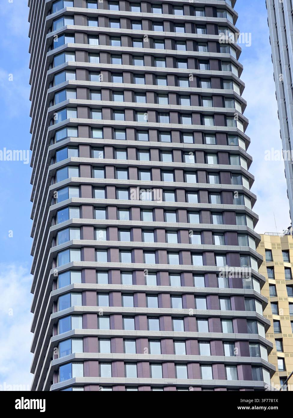 Nahaufnahme eines rechteckigen glänzenden Wolkenkratzers mit moderner Architektur, hohem quadratischem Turm mit abgerundeten Ecken; viele Fenster in einem rechteckigen Muster - Smartphone-aufgenommenes Stockfoto