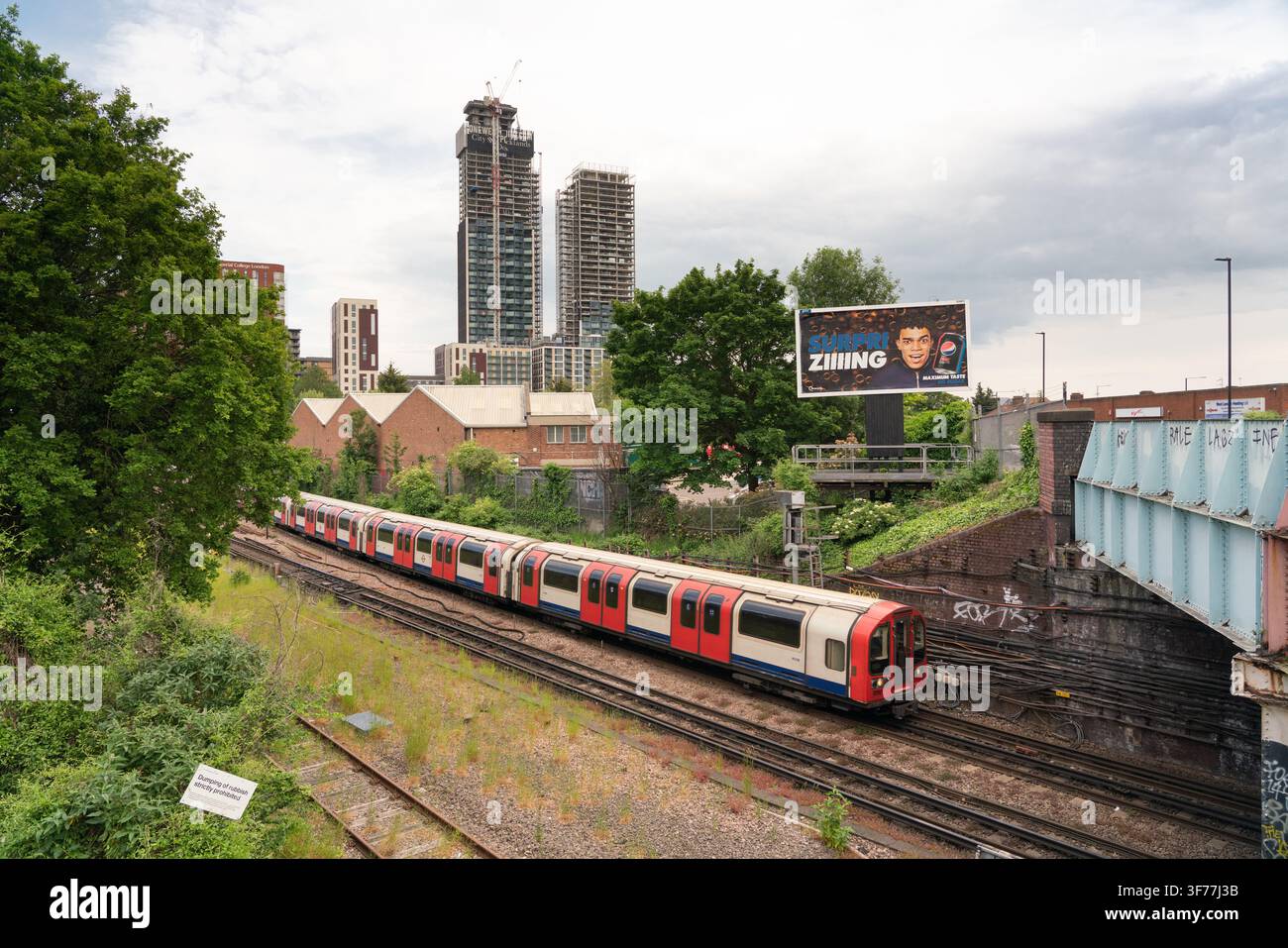 Ein London Underground-Zug fährt durch Park Royal, London, vor dem Hintergrund der One West Point-Hochhausentwicklung. Stockfoto