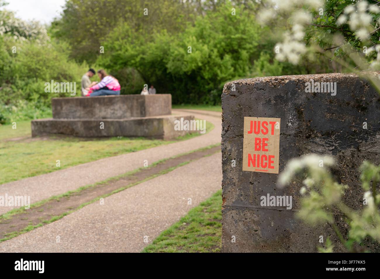Ein "Just Be Nice"-#ReclaimTheNight-Poster an einem WWII-Bunker im Haggerston Park, London, während Besucher sich auf der historischen Struktur entspannen. Stockfoto