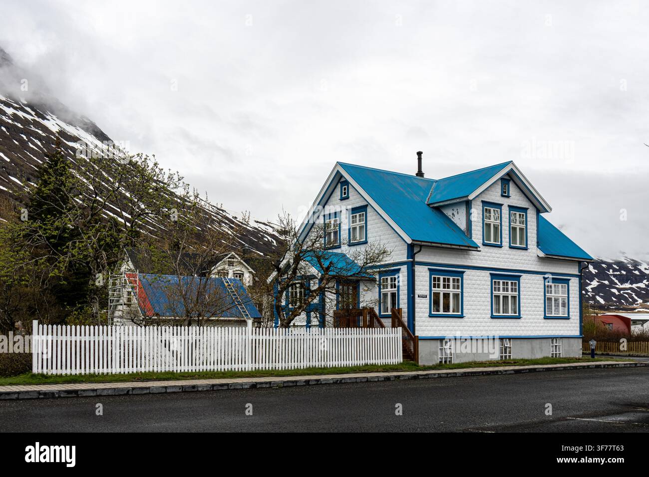 Traditionelles skandinavisches Wellblechhaus unter bewölktem Himmel mit schneebedecktem Berghintergrund in Seydisfjordur Ostisland Island Stockfoto