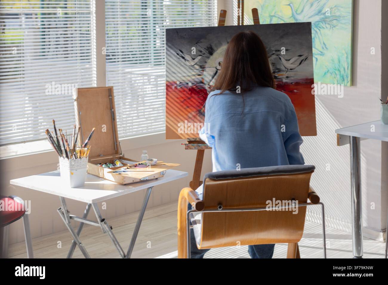 Female artist painting on canvas in a bright home studio with natural sunlight, art supplies and creative workspace. Stockfoto