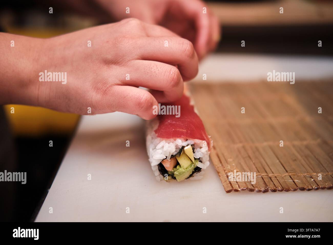 Hände bereiten köstliche japanische Sushi-Rolle mit Thunfisch, Reis und frischen Zutaten zu Stockfoto