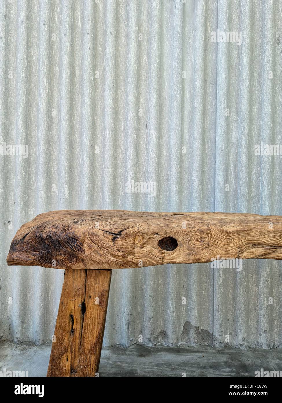 Rustikische Bank aus massivem Holz mit natürlicher Holzmaserung und Astloch vor Hintergrund einer Wellblechwand - Smartphone-aufgenommenes Stockfoto