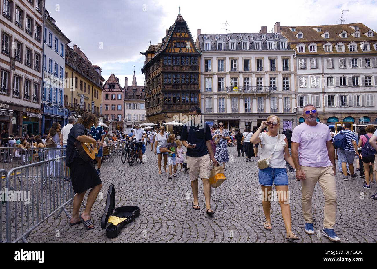 STRASBOURG, FRANKREICH - 6. AUGUST 2026 - Menschen gehen auf einem Kopfsteinpflasterplatz in Straßburg, während ein Straßenmusiker auftritt Stockfoto