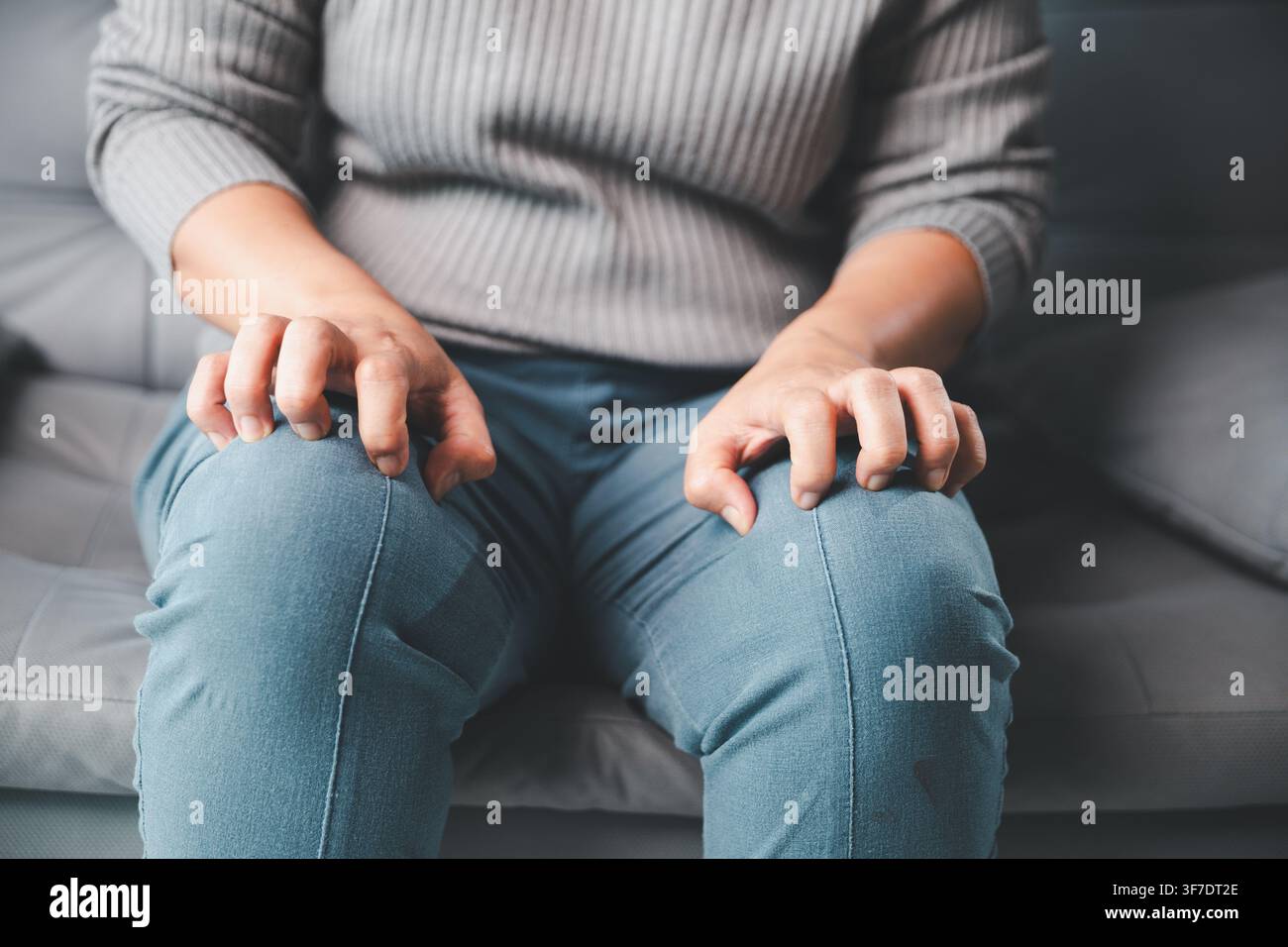 Nahaufnahme eines ängstlichen Erwachsenen, der beide Knie umklammert, während er auf einem Sofa sitzt, und nervöse Anspannung, Unruhe, Angst und emotionalen Unbehaglichkeit zeigt Stockfoto