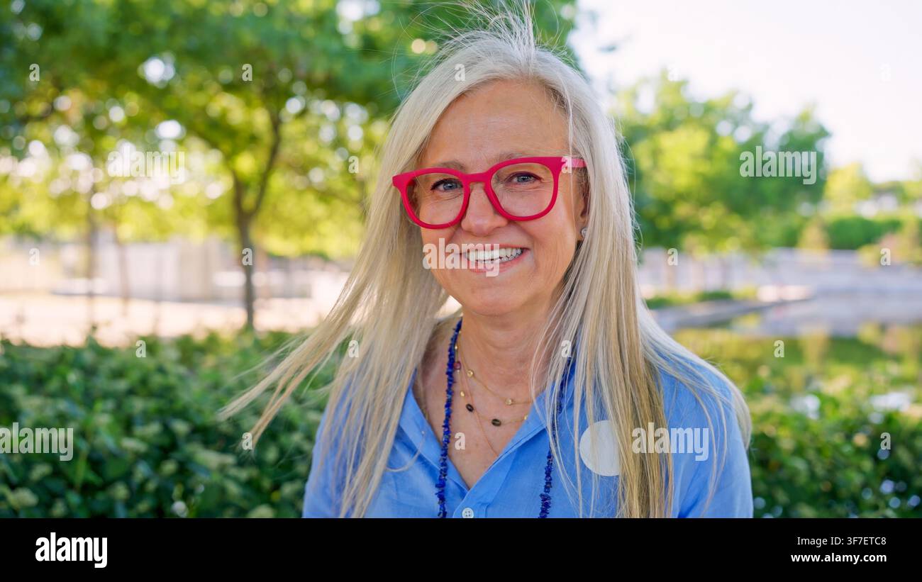 Seniorin mit roter Brille lächelt im Park Stockfoto