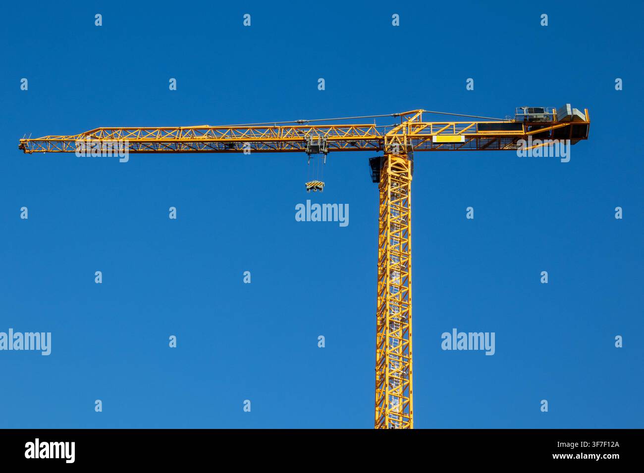 Gelber Turmdrehkran im Profil mit Ausleger, Gegenausleger und Haken vor klarem Himmel Stockfoto