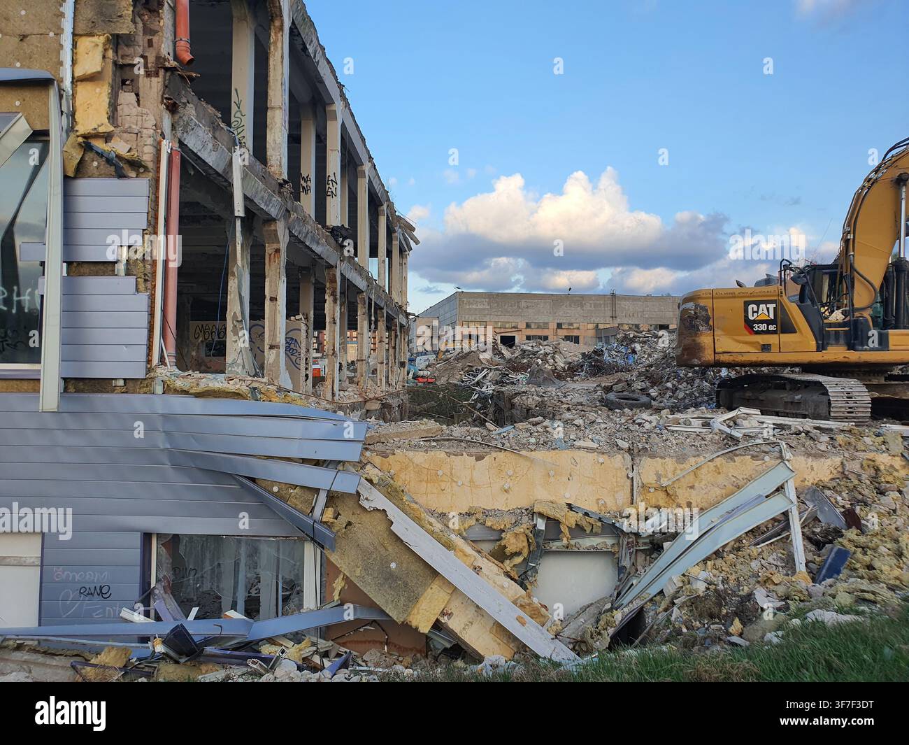 Eine Abbruchstätte mit einem teilweise abgerissenen mehrstöckigen Industriegebäude mit freiliegenden Betonstützen, zerbrochenen Fenstern und verstreuten Stockfoto