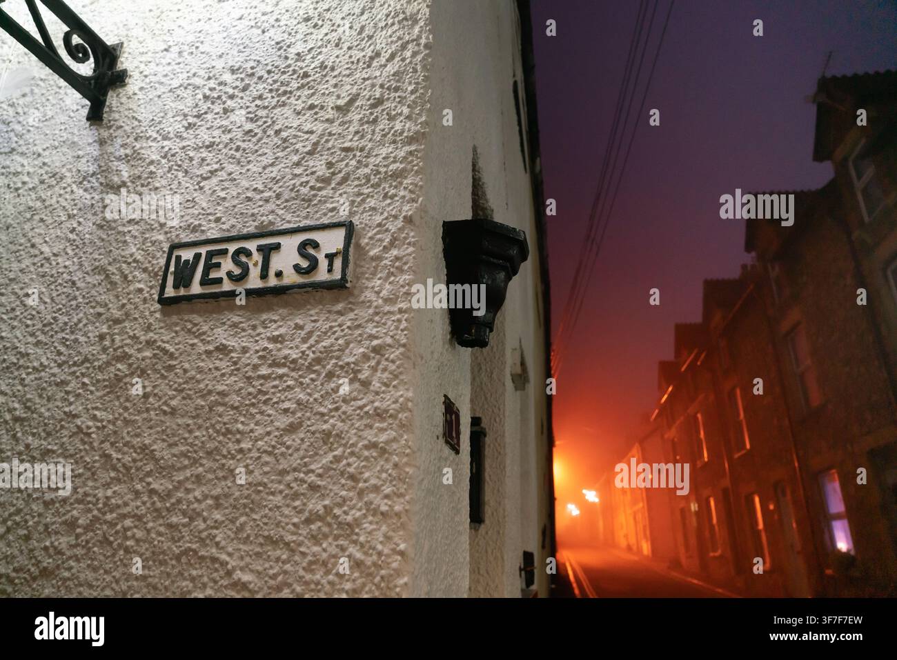 Atmosphärischer Nachttau bedeckt West Street in Watchet, Somerset, und beleuchtet das historische Straßenschild in einem unheimlichen, stimmungsvollen Schein. Stockfoto