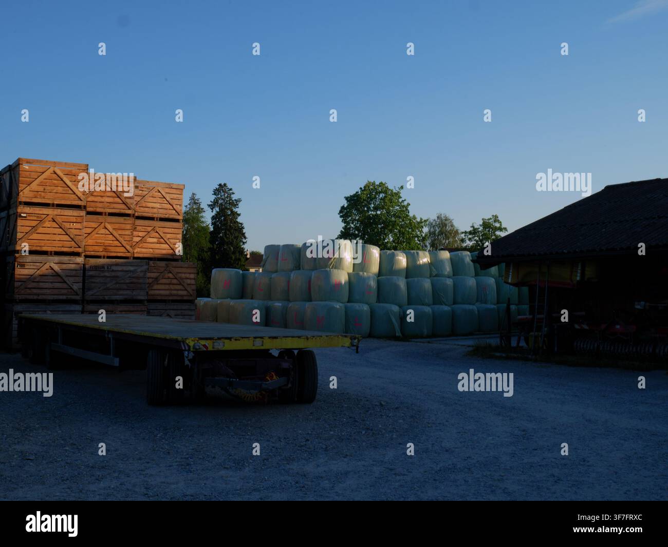 Bauernhof mit gestapelten Holzverschlägen, eingewickelten Heuballen und einem Pritschenanhänger auf einem ländlichen landwirtschaftlichen Grundstück Stockfoto