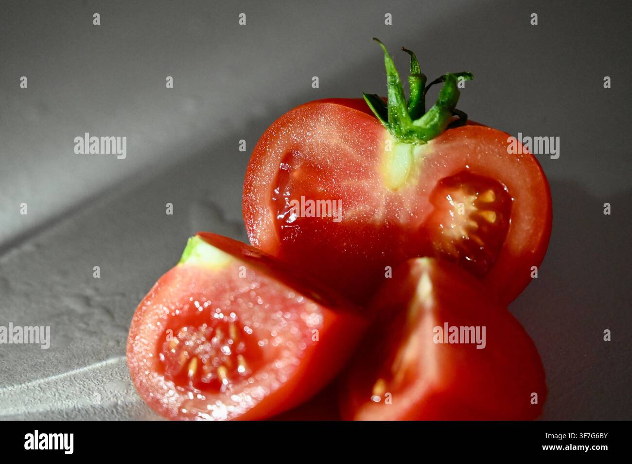 Nahaufnahme eines kommerziellen Fotos einer frischen reifen roten Tomate, die in Hälften und Keile geschnitten ist, mit sichtbaren Samen und grünem Stiel. Geeignet für Konzepte rund um gesunde Ernährung, saubere Ernährung, Bio-Gemüse, Kochzutaten, vegetarische Lebensmittel und frische Produkte. Stockfoto