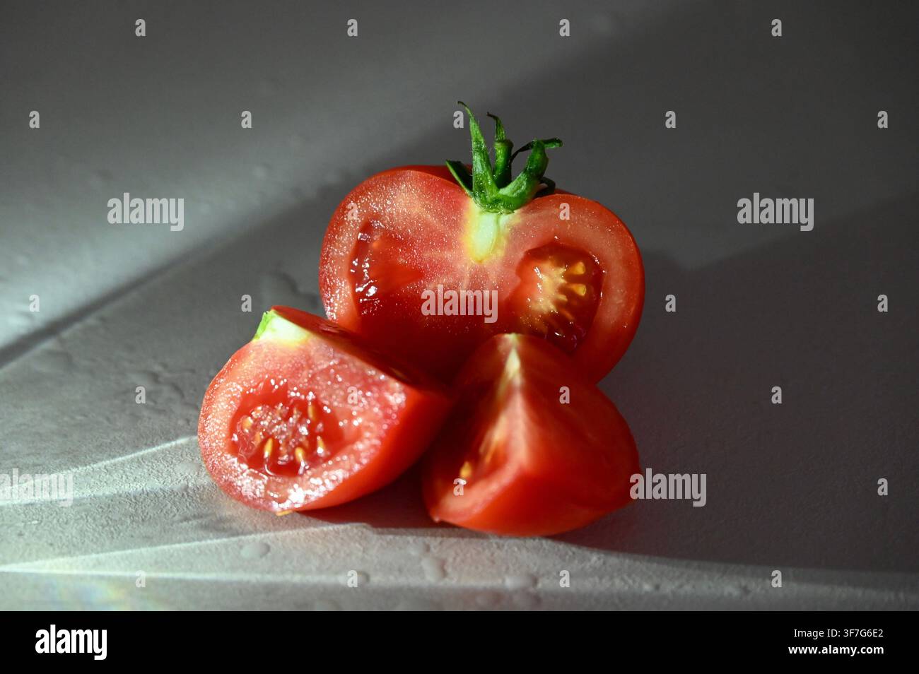 Nahaufnahme eines kommerziellen Fotos einer frischen reifen roten Tomate, die in Hälften und Keile geschnitten ist, mit sichtbaren Samen und grünem Stiel. Geeignet für Konzepte rund um gesunde Ernährung, saubere Ernährung, Bio-Gemüse, Kochzutaten, vegetarische Lebensmittel und frische Produkte. Stockfoto