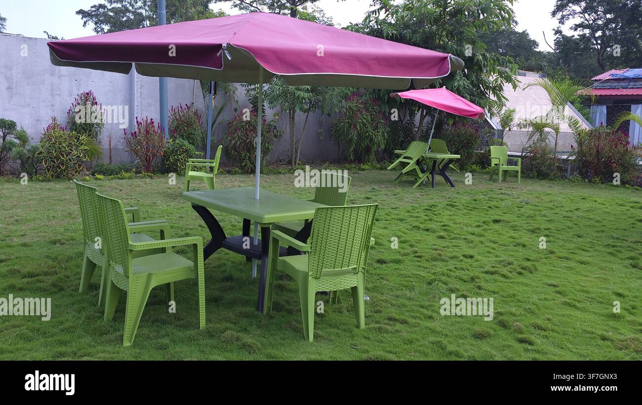 Garten-Essbereich im Freien mit rosa Sonnenschirmen und grünen Plastikstühlen Stockfoto