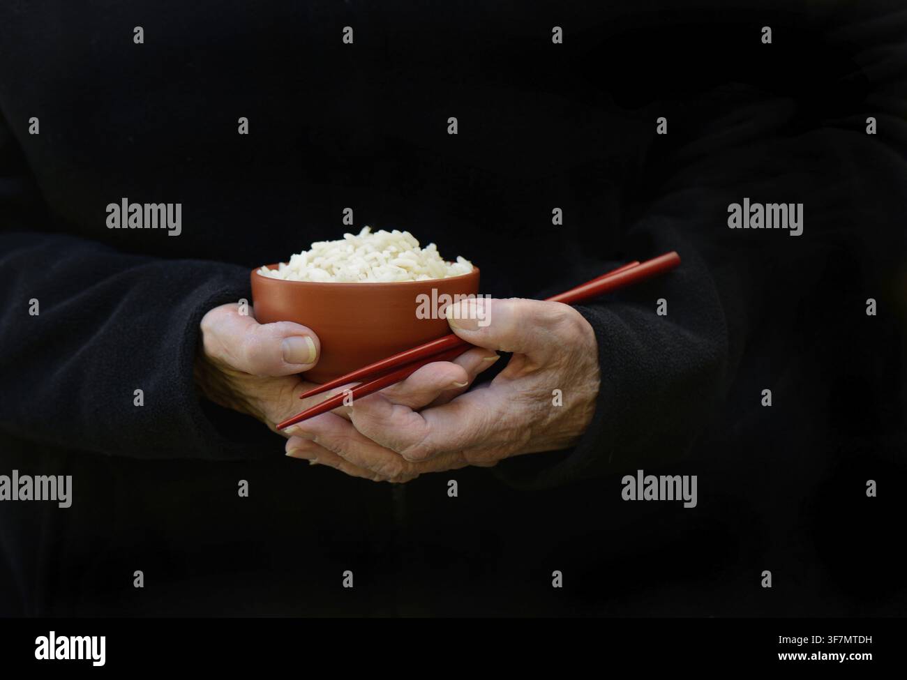 Hand hält eine Schüssel mit Reis und Essstäbchen, dunkler Hintergrund Stockfoto