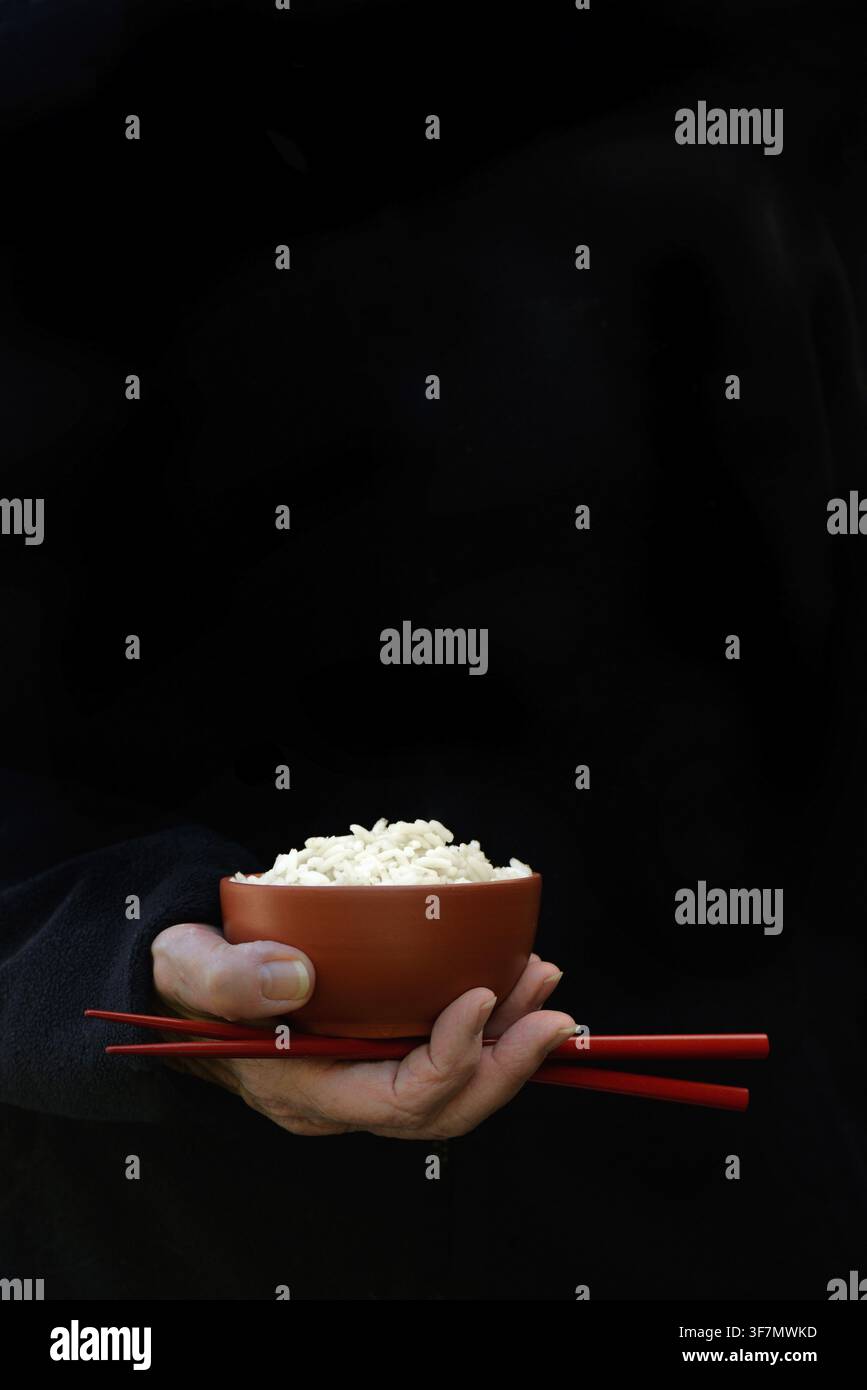 Hand hält eine Schüssel mit Reis und Essstäbchen, dunkler Hintergrund Stockfoto