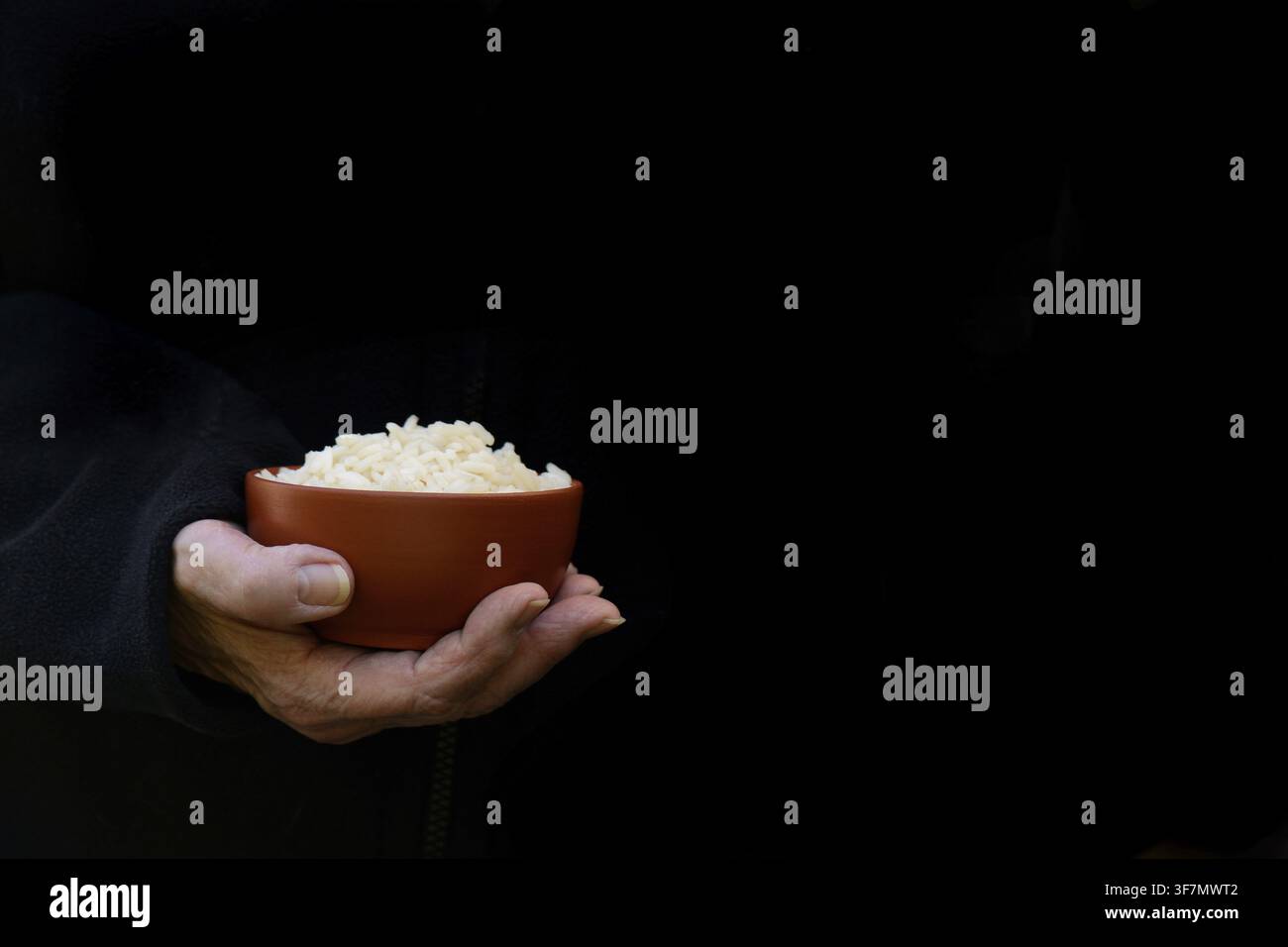 Hand hält eine Schüssel Reis vor dunklem Hintergrund Stockfoto