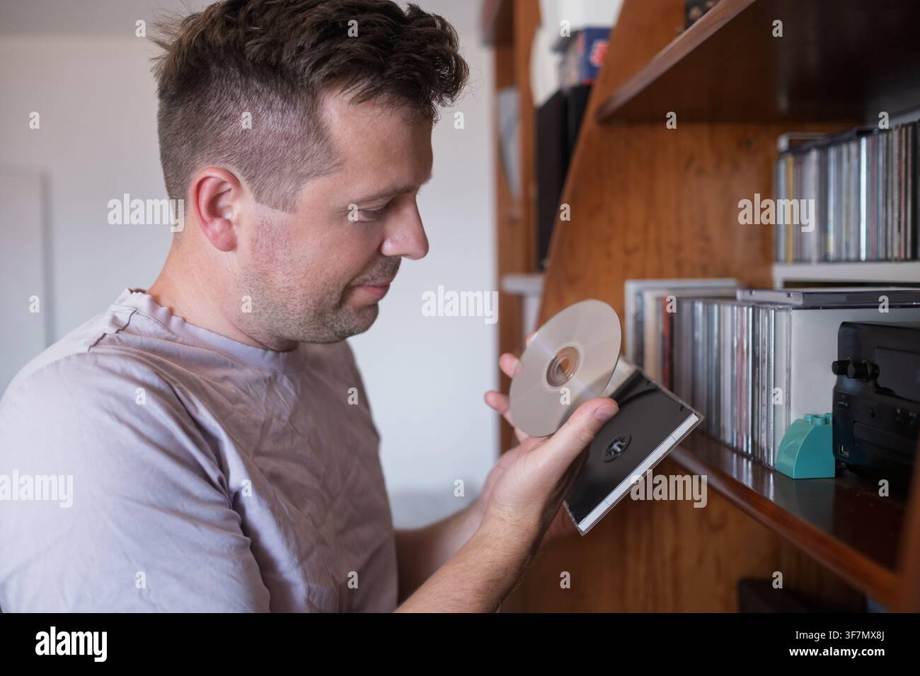 Mann hält eine Compact Disc in der Nähe eines Regals mit Musiksammlung Stockfoto