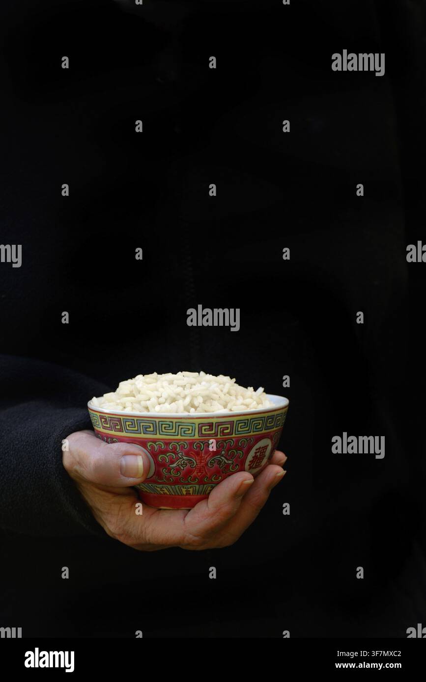Hand hält eine Schüssel Reis vor dunklem Hintergrund Stockfoto