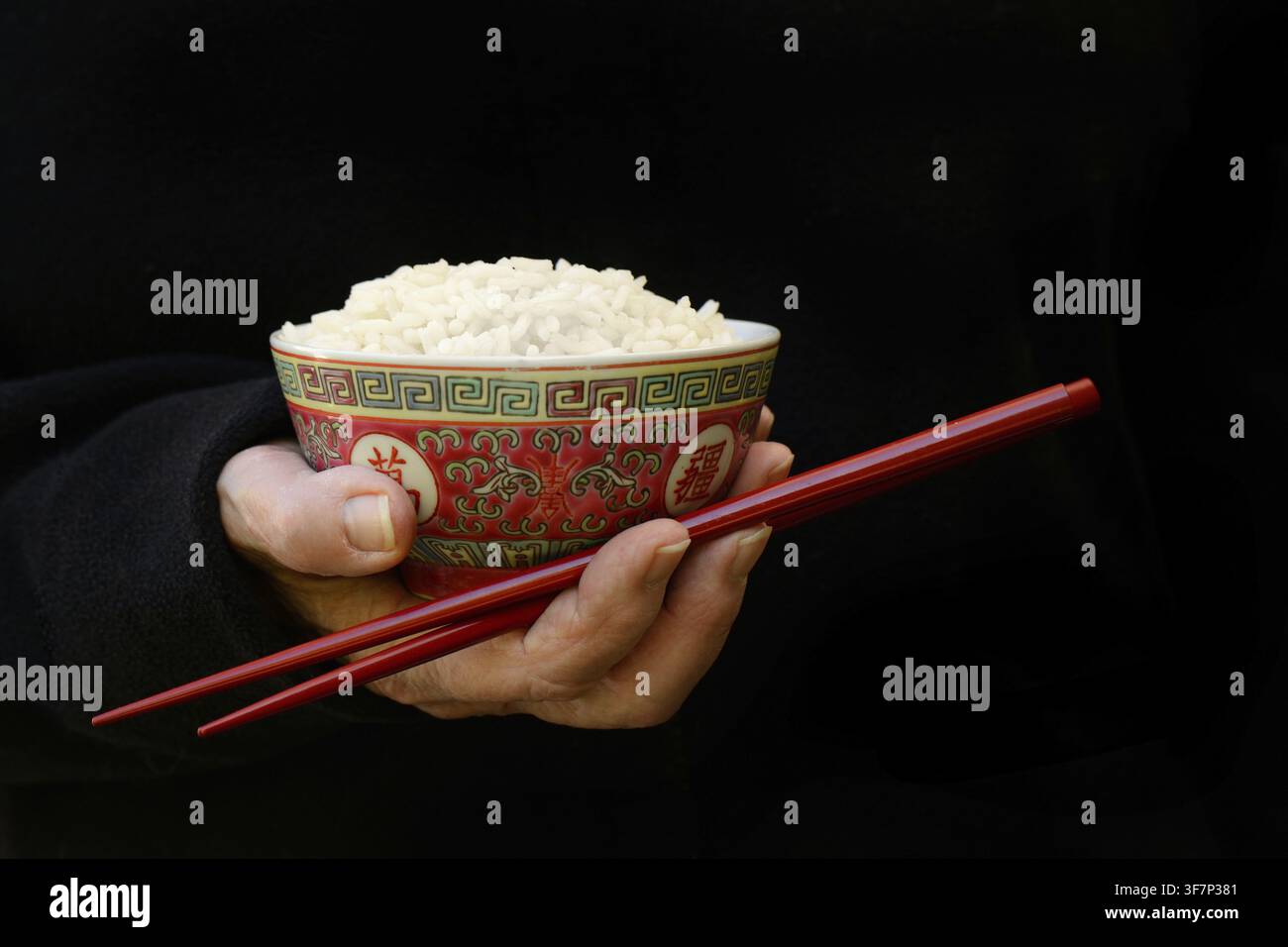 Hand hält eine Schüssel mit Reis und Essstäbchen, dunkler Hintergrund Stockfoto