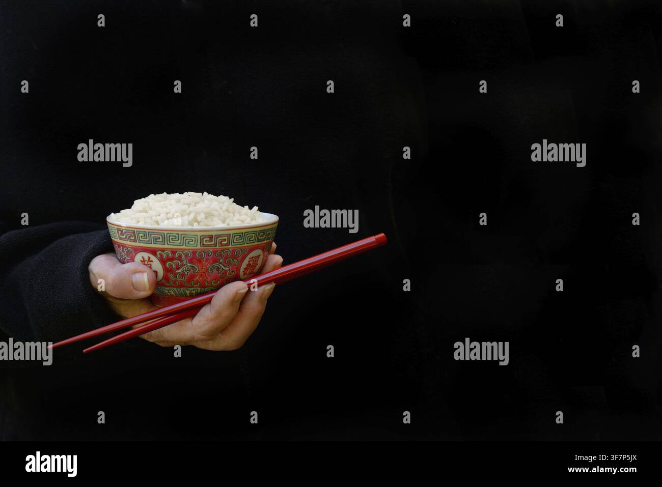 Hand hält eine Schüssel mit Reis und Essstäbchen, dunkler Hintergrund Stockfoto