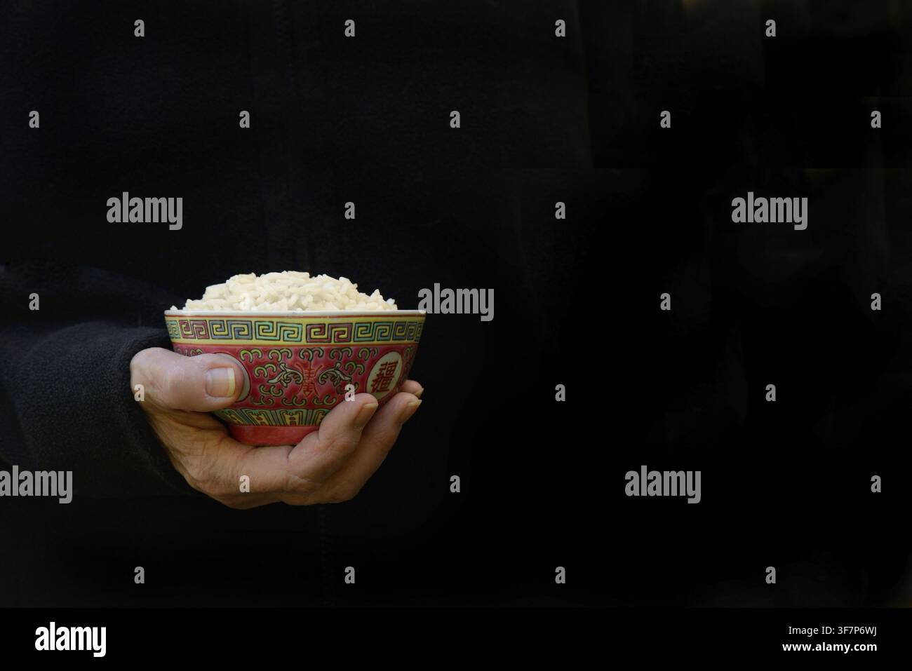 Hand hält eine Schüssel Reis vor dunklem Hintergrund Stockfoto