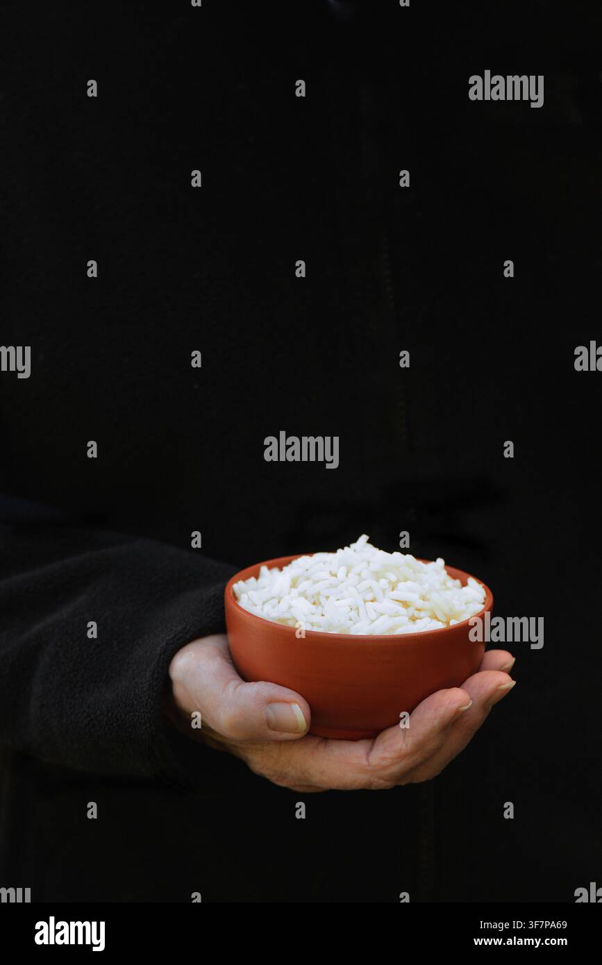 Hand hält eine Schüssel Reis vor dunklem Hintergrund Stockfoto