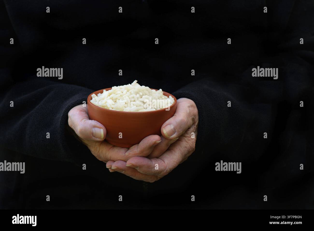 Hand hält eine Schüssel Reis vor dunklem Hintergrund Stockfoto