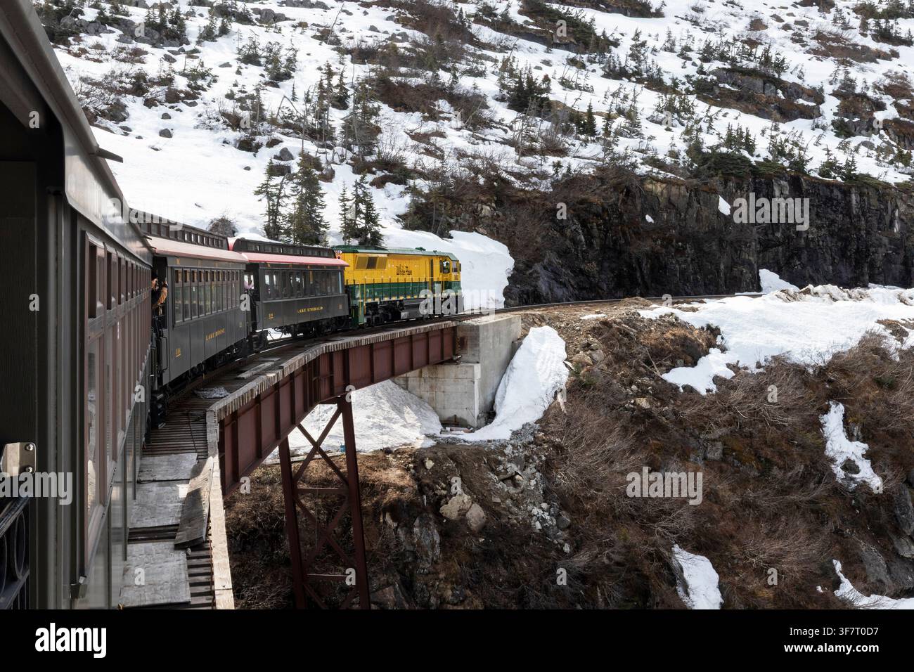 Die White Pass & Yukon Route-Lokomotive 3002 zieht einen Personenzug über eine Stahlträgerbrücke an der Glacier Station in den rauen Bergen abo Stockfoto