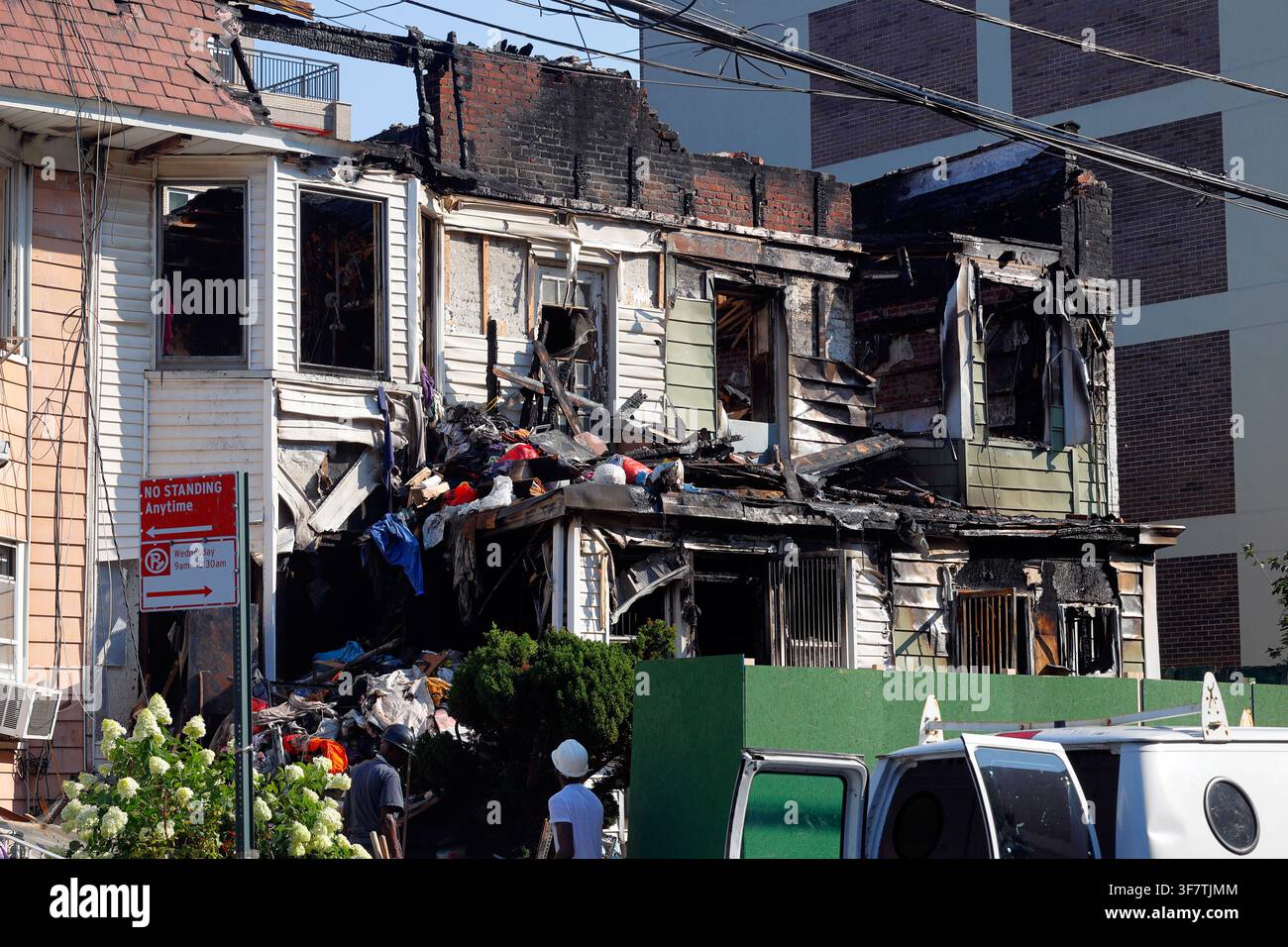 Arbeiter kommen, um aufzuräumen, nachdem ein Feuer an mehreren holzgerahmten Häusern in der 41st Rd in Flushing, Queens County, New York, am 25. Juli 2026 ausgebrochen ist. Stockfoto