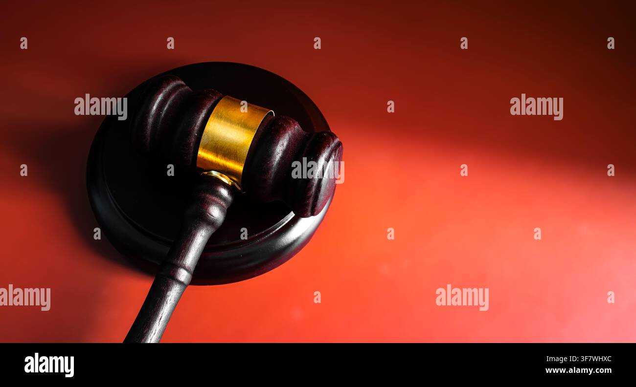 Nahaufnahme eines hölzernen Richterhammer mit goldenem Band auf leuchtend rotem Hintergrund, Konzept für Gerichtsjustiz und rechtliche Autorität Stockfoto