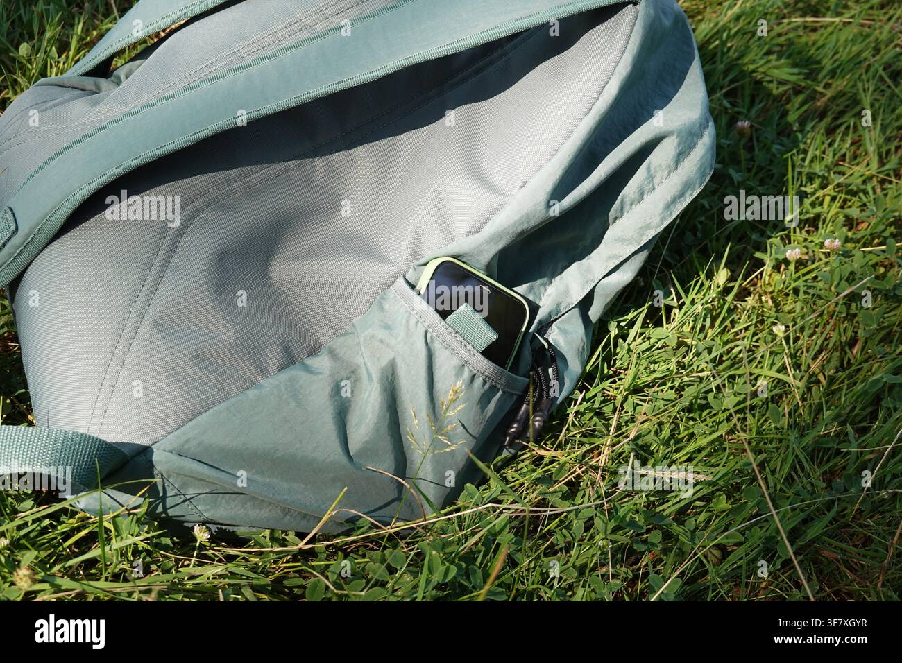 Smartphone verstaut in der grünen Gesäßtasche des Rucksacks, der in der Natur ruht, als Digital-Detox-Konzept Stockfoto