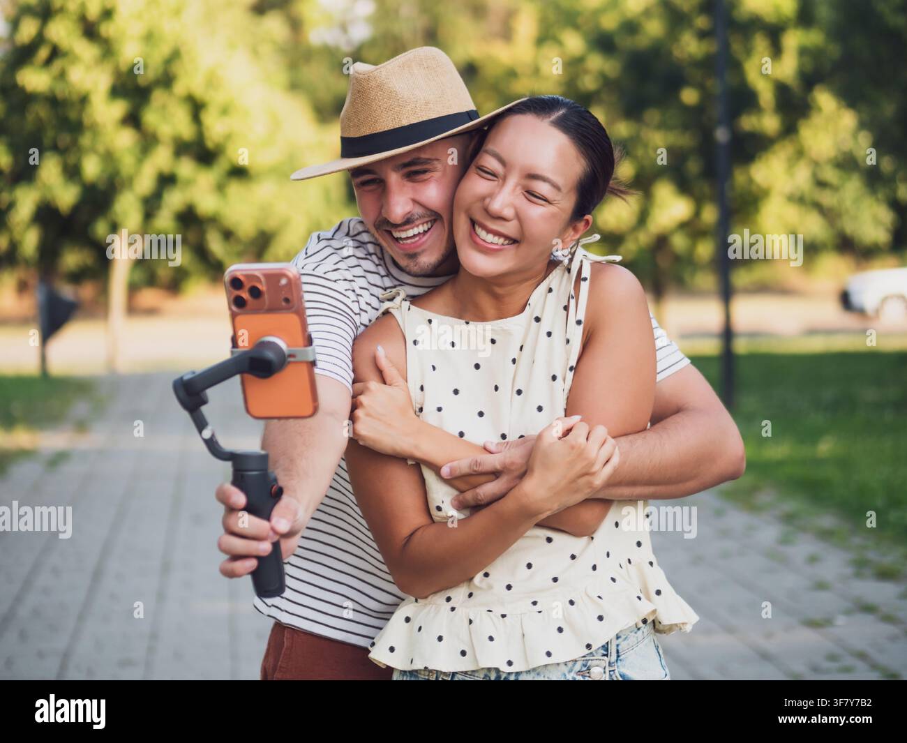Junger Mann umarmt seine Freundin von hinten, während sie einen verspielten Moment zusammen auf einem Smartphone einfangen. Stockfoto