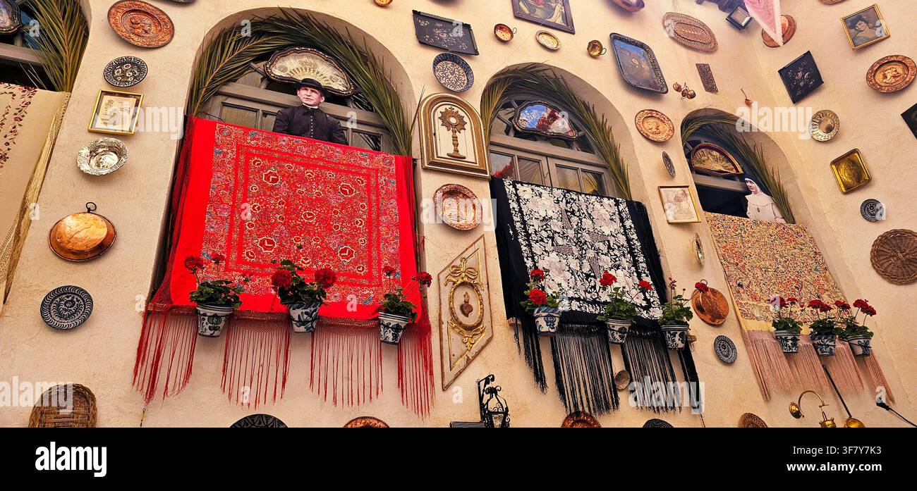 Andalusischer Innenhof, der mit bestickten, fransigen Schals, Keramiktellern, Kupferwaren, Topfgeranien und gerahmten religiösen Bildern während der Cr geschmückt ist Stockfoto