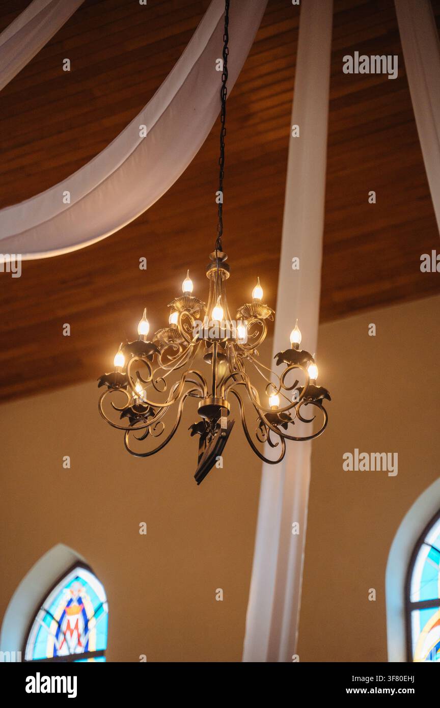 Antiker Luxus-Kronleuchter mit Kerzen, der an einer hohen Decke in einer Kirche hängt, historisches Innendesign. Hochwertiges Foto Stockfoto