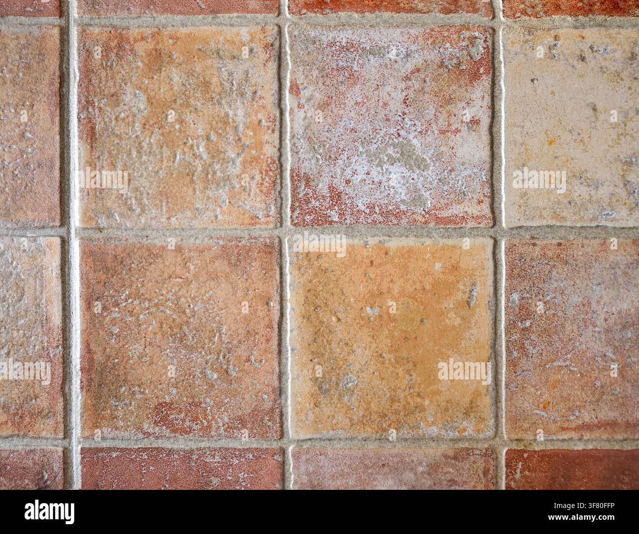 Detail rustikaler Fliesen in verschiedenen Brauntönen, die mit einem breiten grauen Fugenmuster an der Wand platziert sind. Vorderansicht. Stockfoto