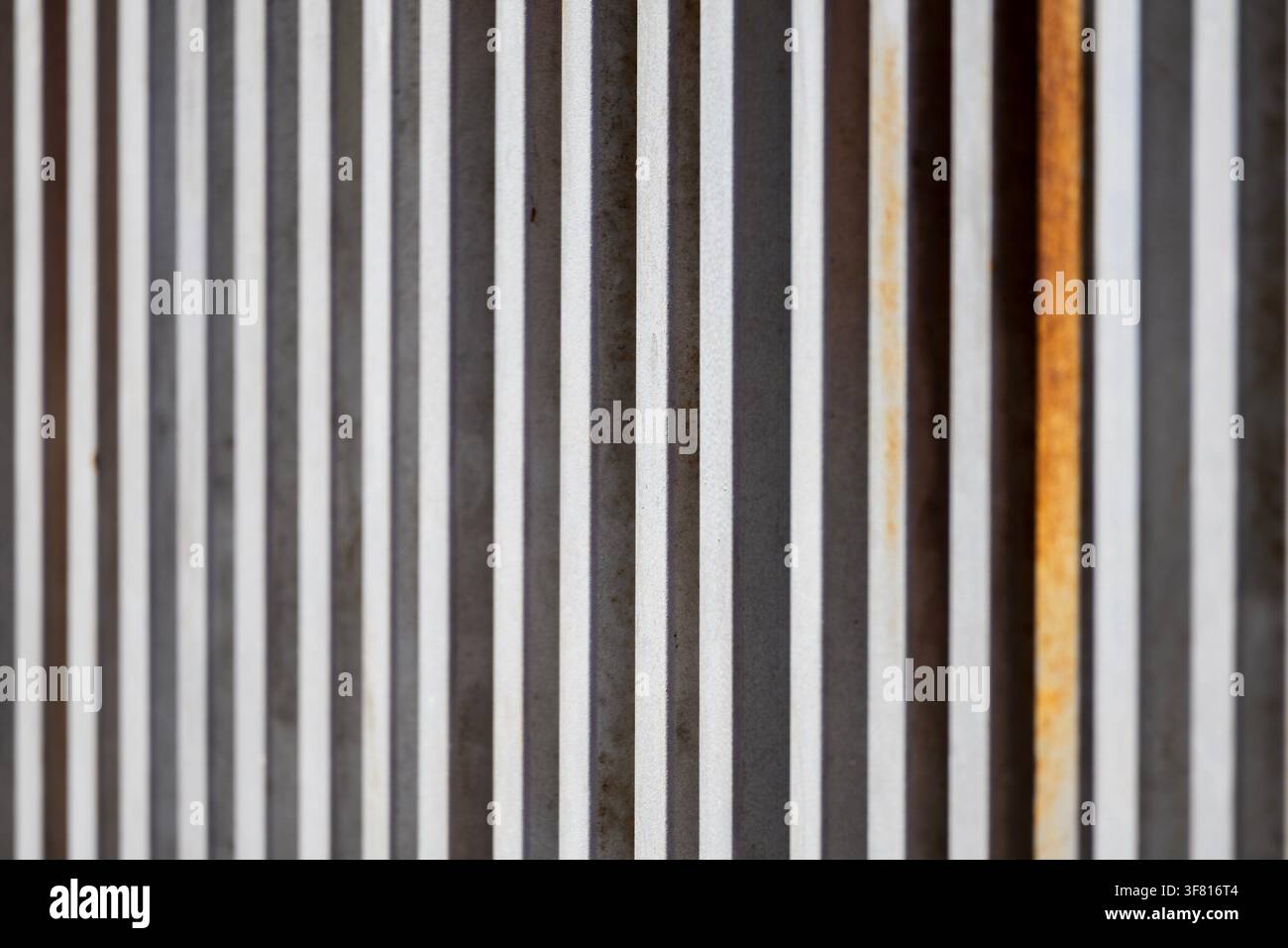 Nahaufnahme eines zeitgenössischen Tores mit vertikalen Metalllamellen in verschiedenen Grautönen und Rost Stockfoto