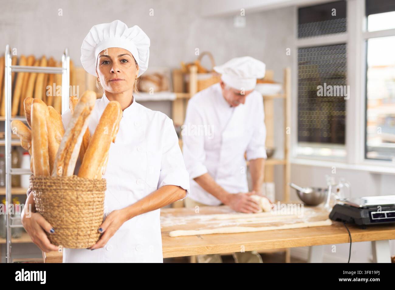 Porträt einer positiven Bäckerin, die einen Korb mit Baguettes und frischem Brot in der Hand hält Stockfoto