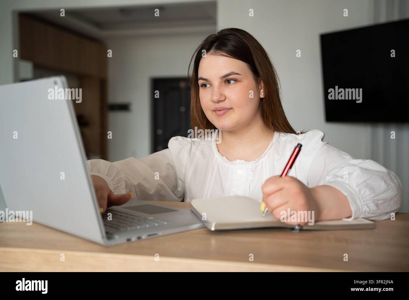 Junge Frau, die einen Laptop benutzt und zu Hause Notizen macht, um das Lernerlebnis zu verbessern. Konzept für Remote-Arbeitsproduktivität und Online-Bildung. Stockfoto
