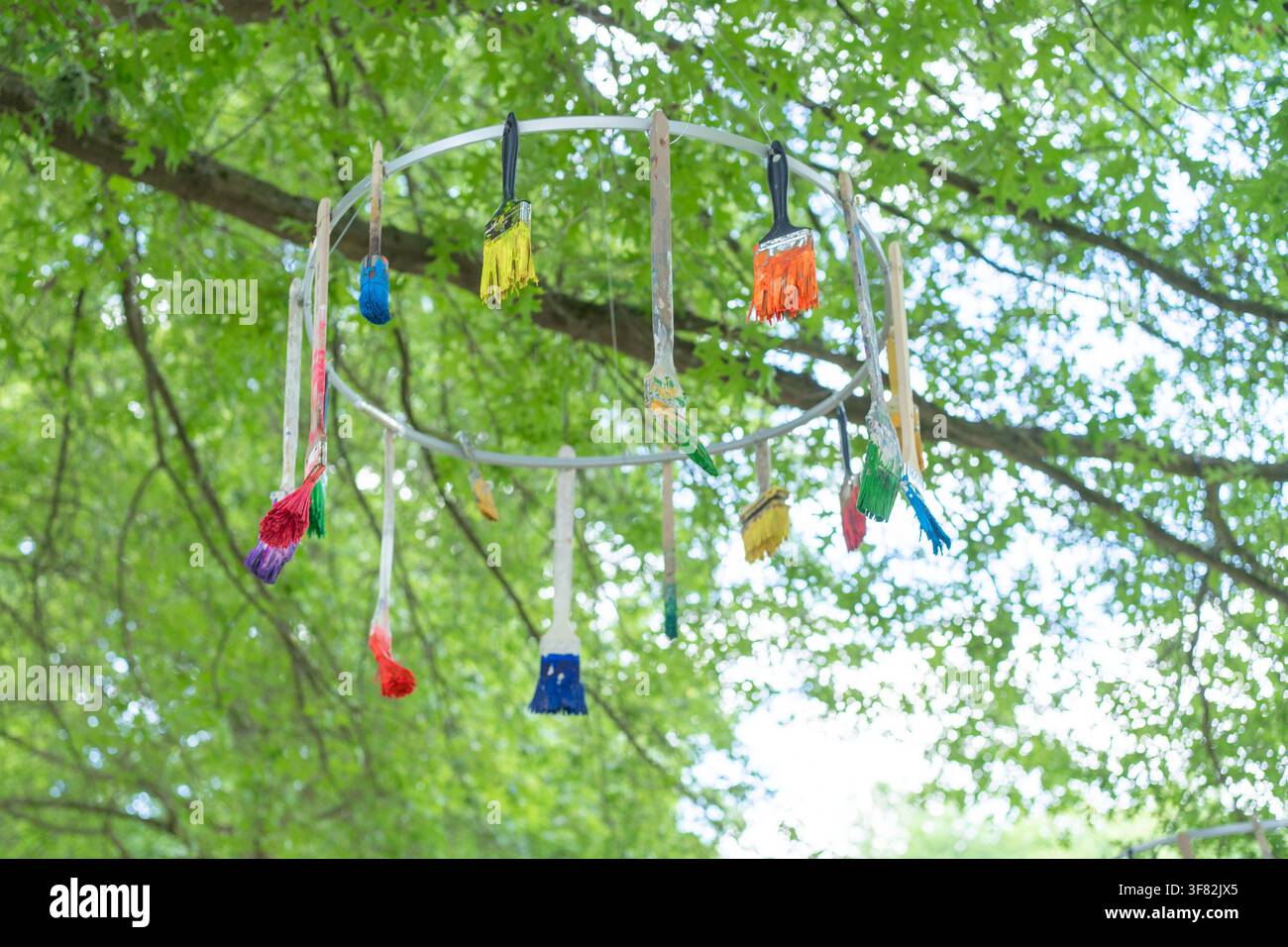 Eine bezaubernde Außendarstellung von Pinsel mit Holzgriffen und synthetischen Borsten, die unter einem Baum auf spielerische und kreative Weise aufgehängt sind Stockfoto