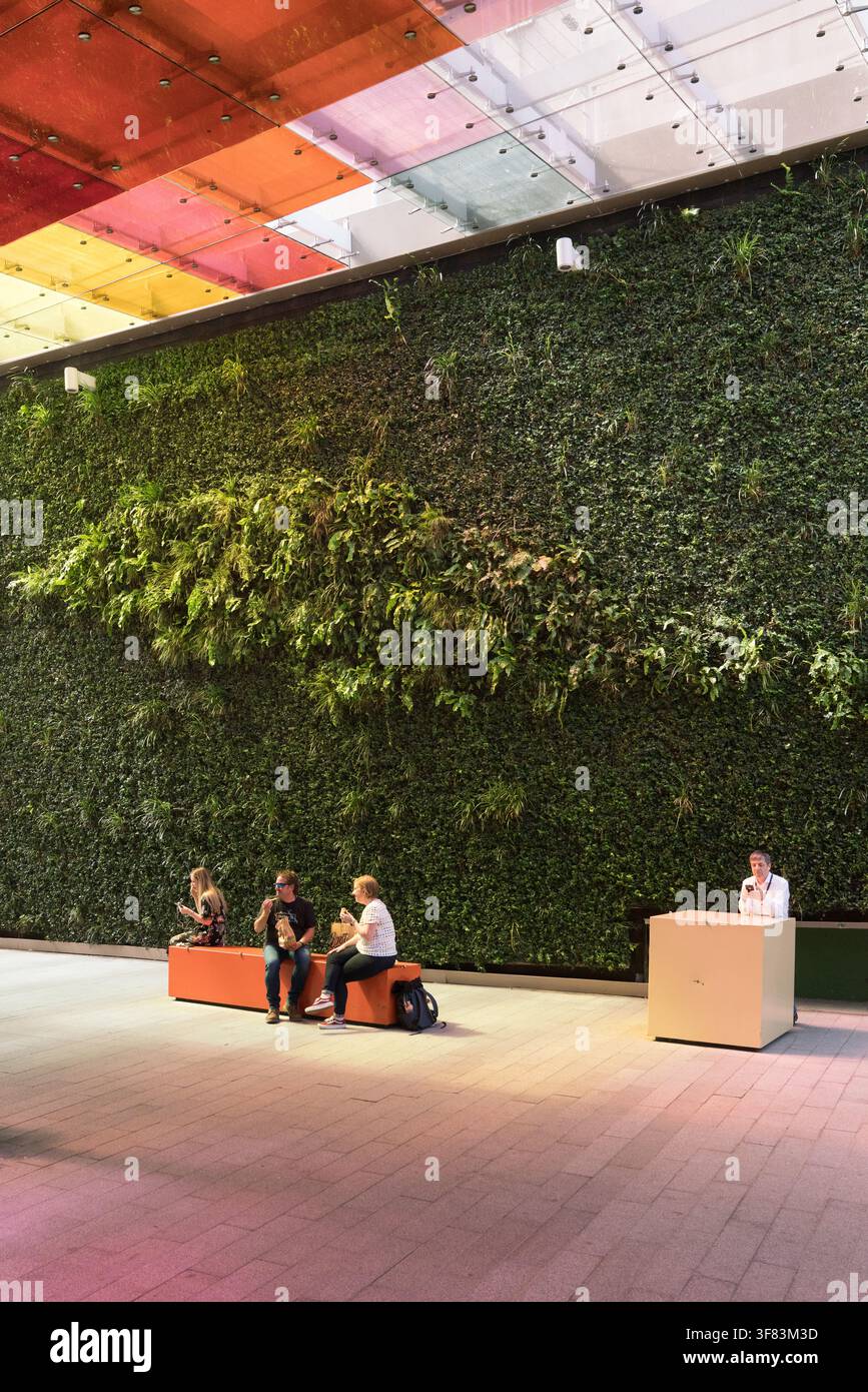 Menschen entspannen sich an der lebenden Wand des Cardinal Place auf dem Seaforth Place in Victoria und genießen eine ruhige städtische Oase unter einem farbenfrohen Glasdach. Stockfoto