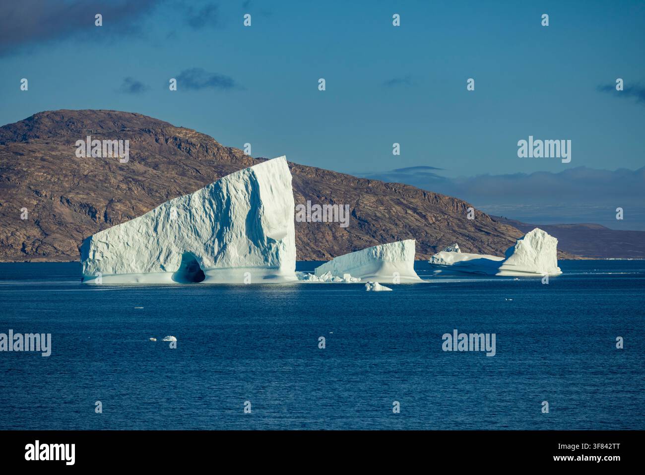 Mächtige Eisberge treiben über tiefblaue Meere in der Nähe von Bjorneoer im arktischen Licht unter klarem Himmel Stockfoto