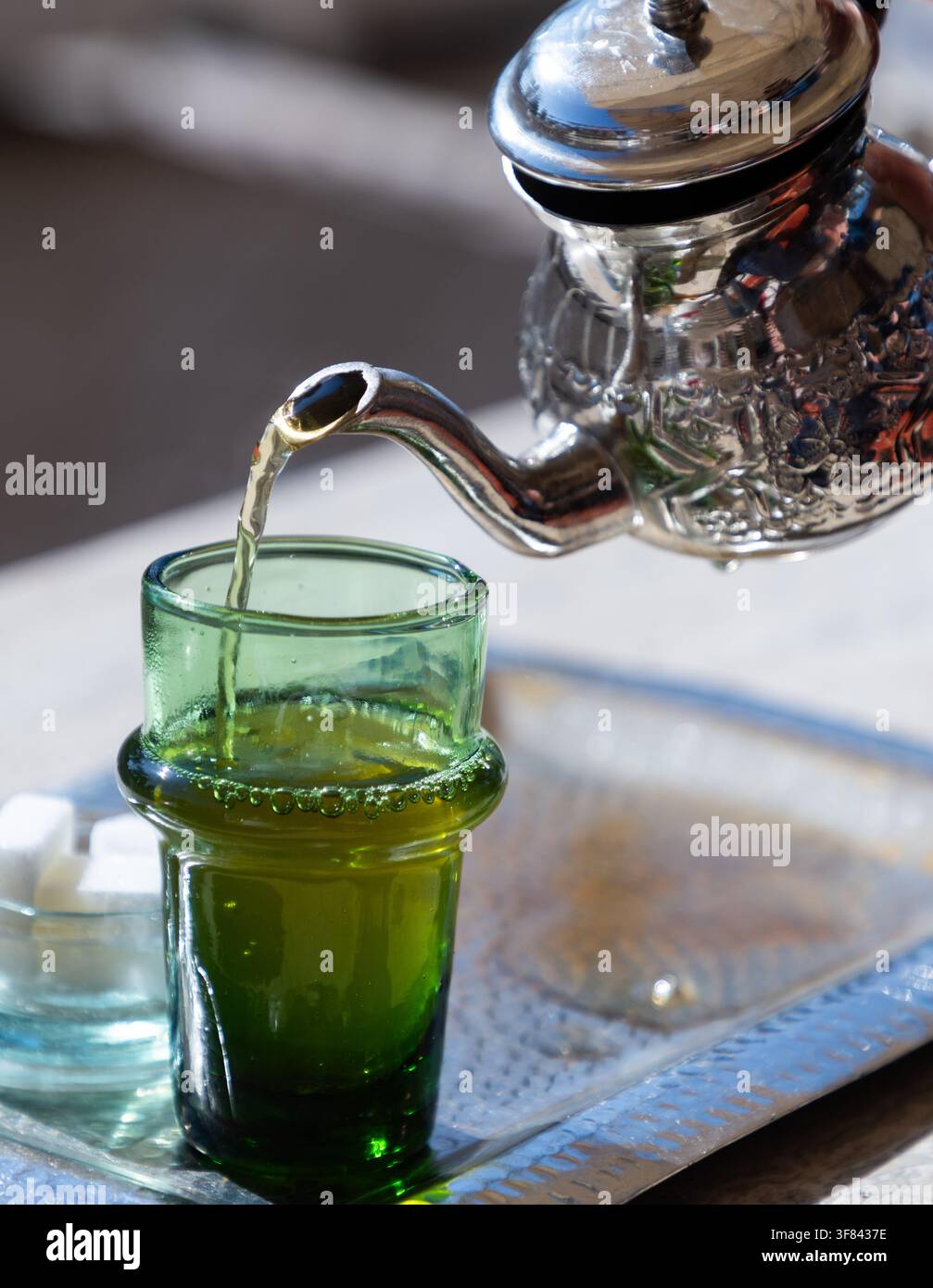 Traditioneller Minztee, serviert in einer silbernen Teekanne mit Zuckerwürfeln auf einem Metalltablett in einer marokkanischen Umgebung Stockfoto